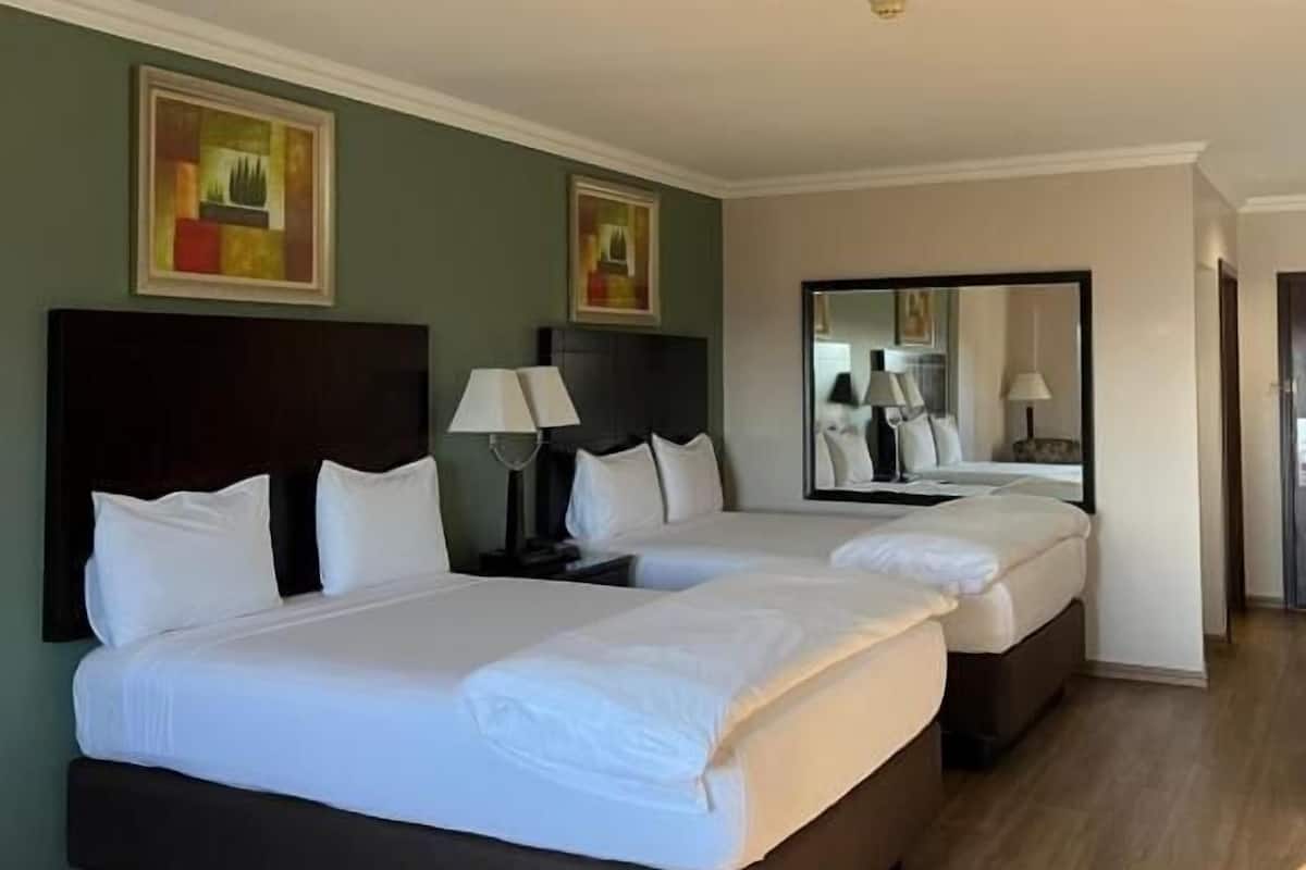 Habitación de hotel con dos camas, un espejo grande y obras de arte en las paredes.