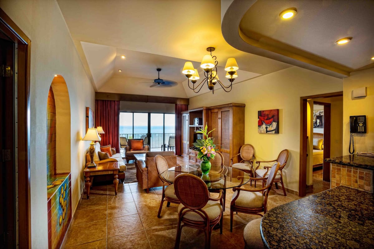 A spacious living area with a dining table, chairs, a sofa, and a view of the ocean.