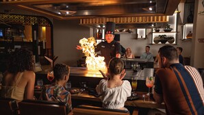 Ravintola, jossa kokki esiintyy tulen kanssa, asiakkaat istuvat pöytien ääressä ja taustalla on baaritiski.