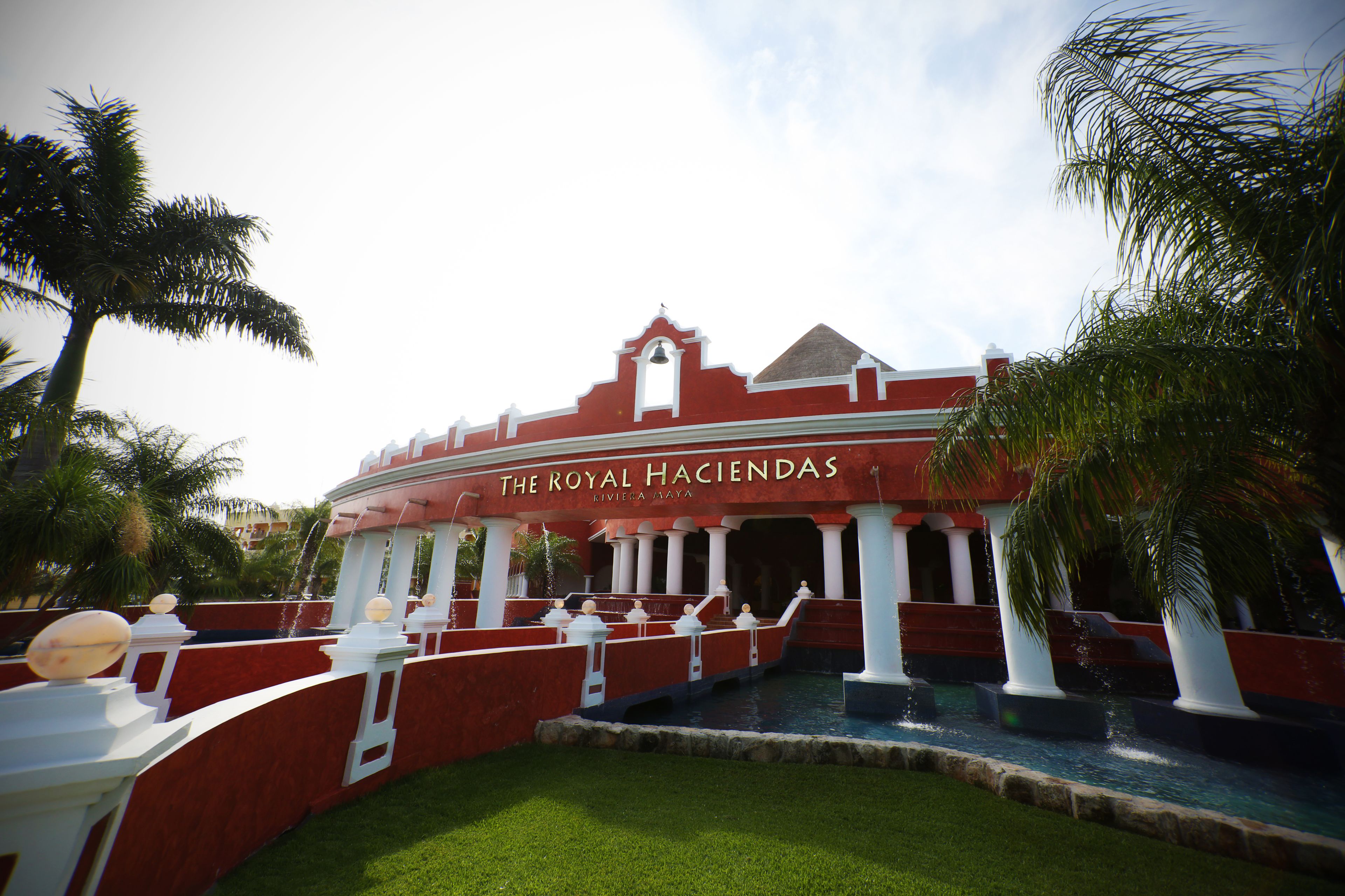 The Royal Haciendas, ein Resort mit einem zentralen Wasserspiel, weißen Säulen und einer roten Fassade.