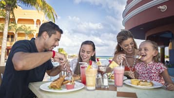 A family dining at an outdoor table with a view of the ocean and palm trees.