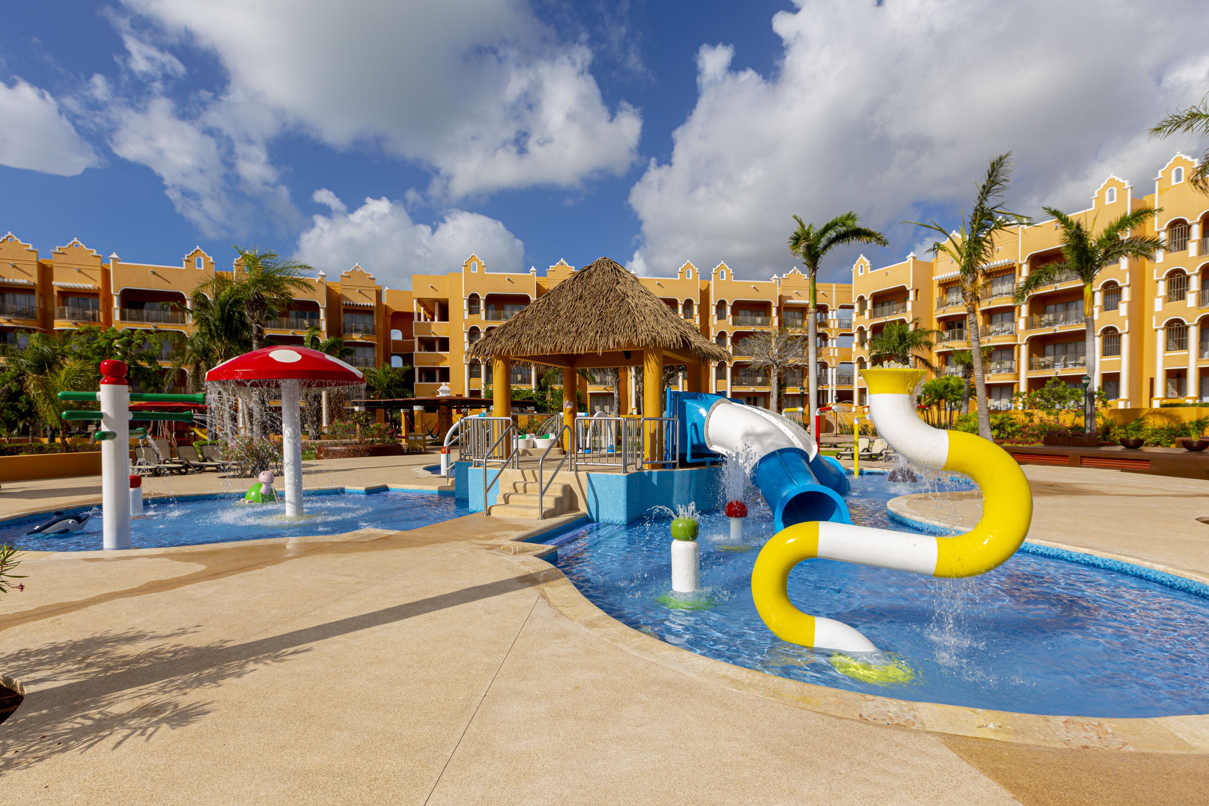 A water park with slides and a pool, surrounded by a resort building with balconies and palm trees.