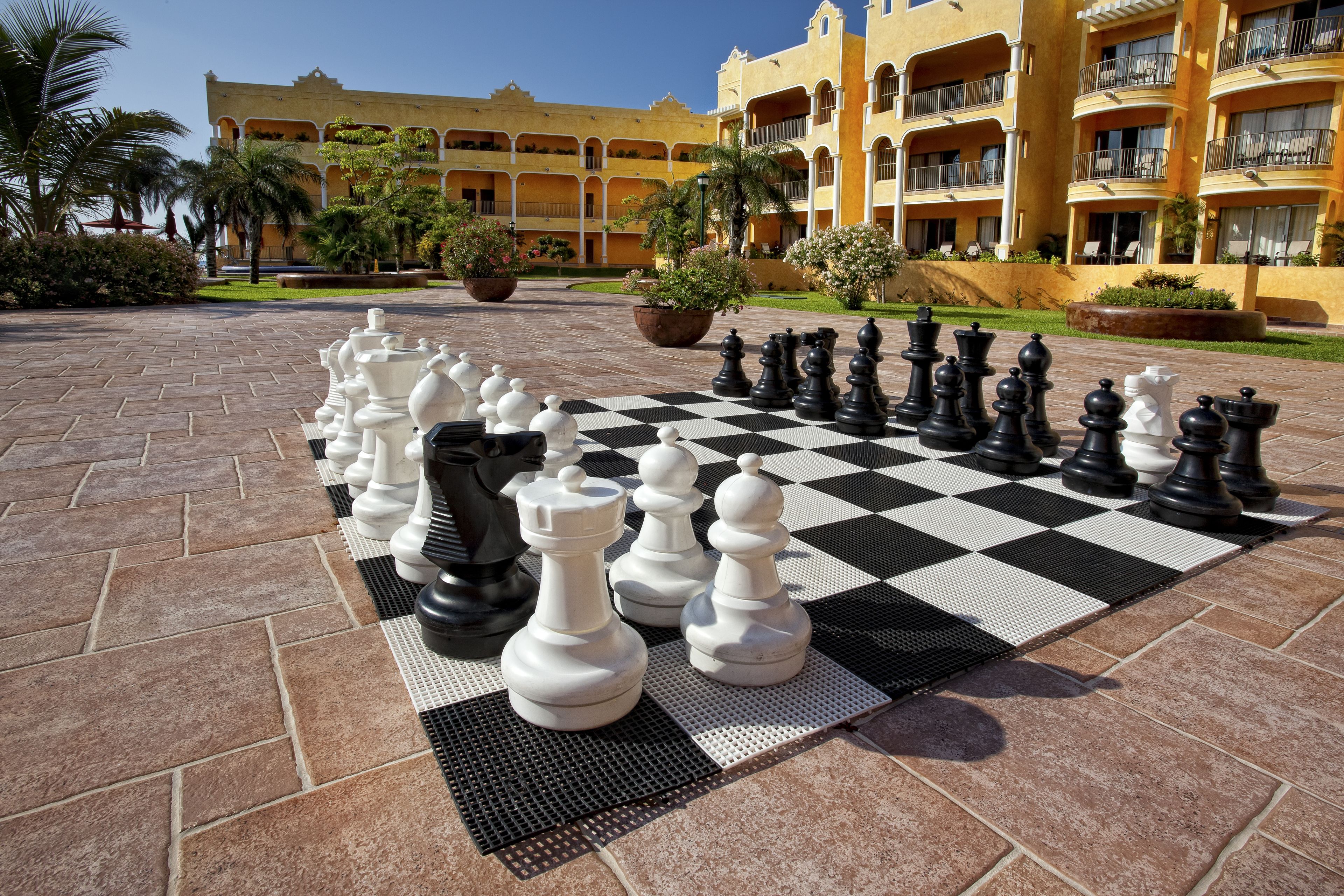Un grand jeu d’échecs en plein air installé dans une cour, avec un bâtiment d’hôtel en arrière-plan.