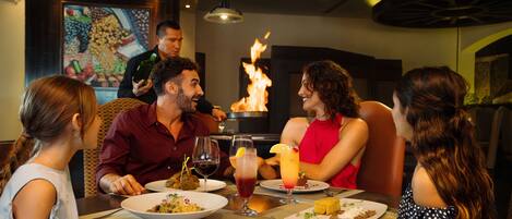 Un grupo de personas cenando en un restaurante con una chimenea central.