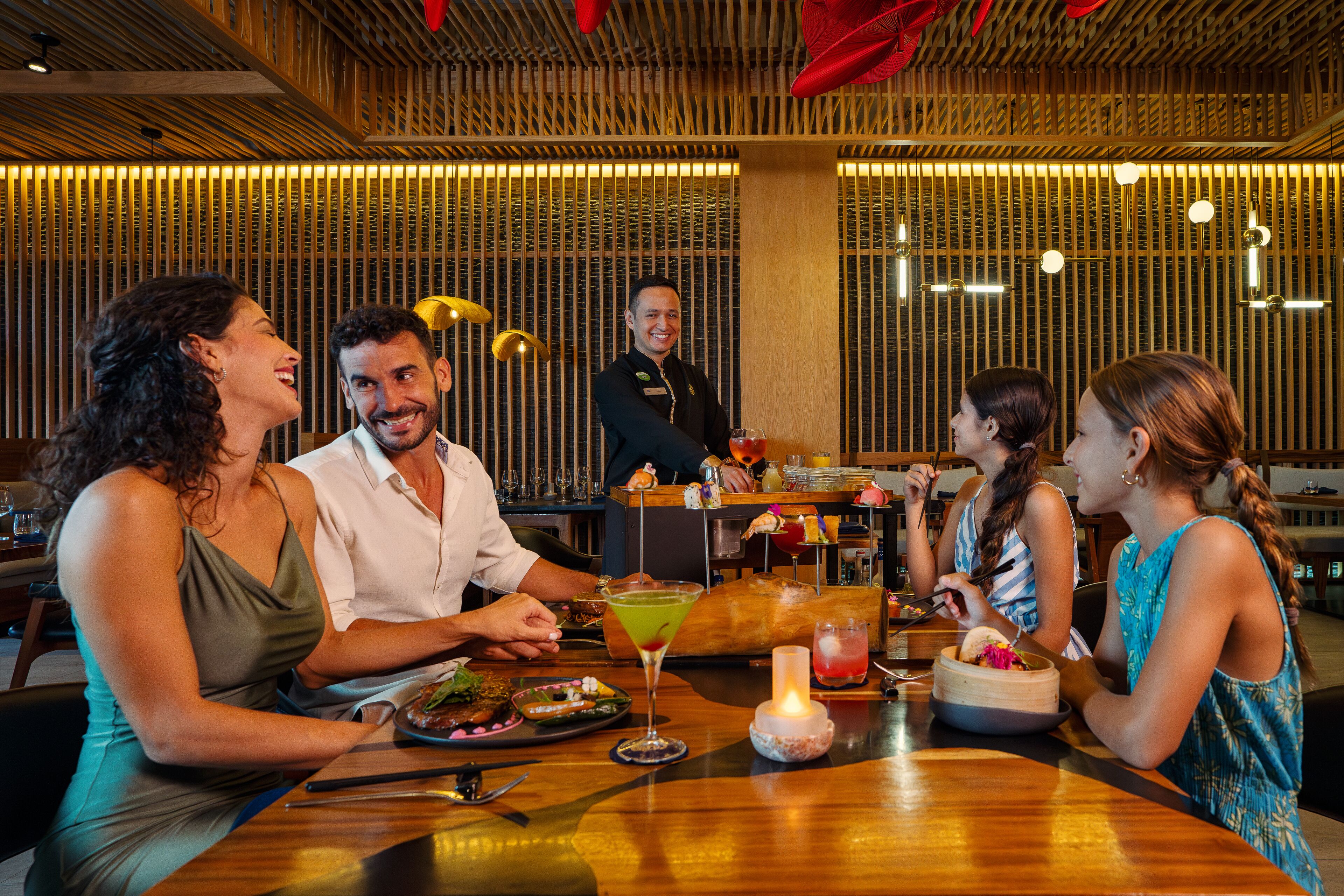 Un grupo de personas cenando en un restaurante con decoración de madera y una barra de bar al fondo.