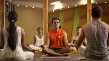 Un grupo de personas sentadas con las piernas cruzadas sobre esterillas de yoga en una habitación con pilares de madera y un espejo en la pared.