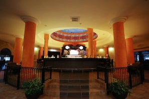 Una hall con una reception centrale, ampie colonne e un soffitto decorativo.
