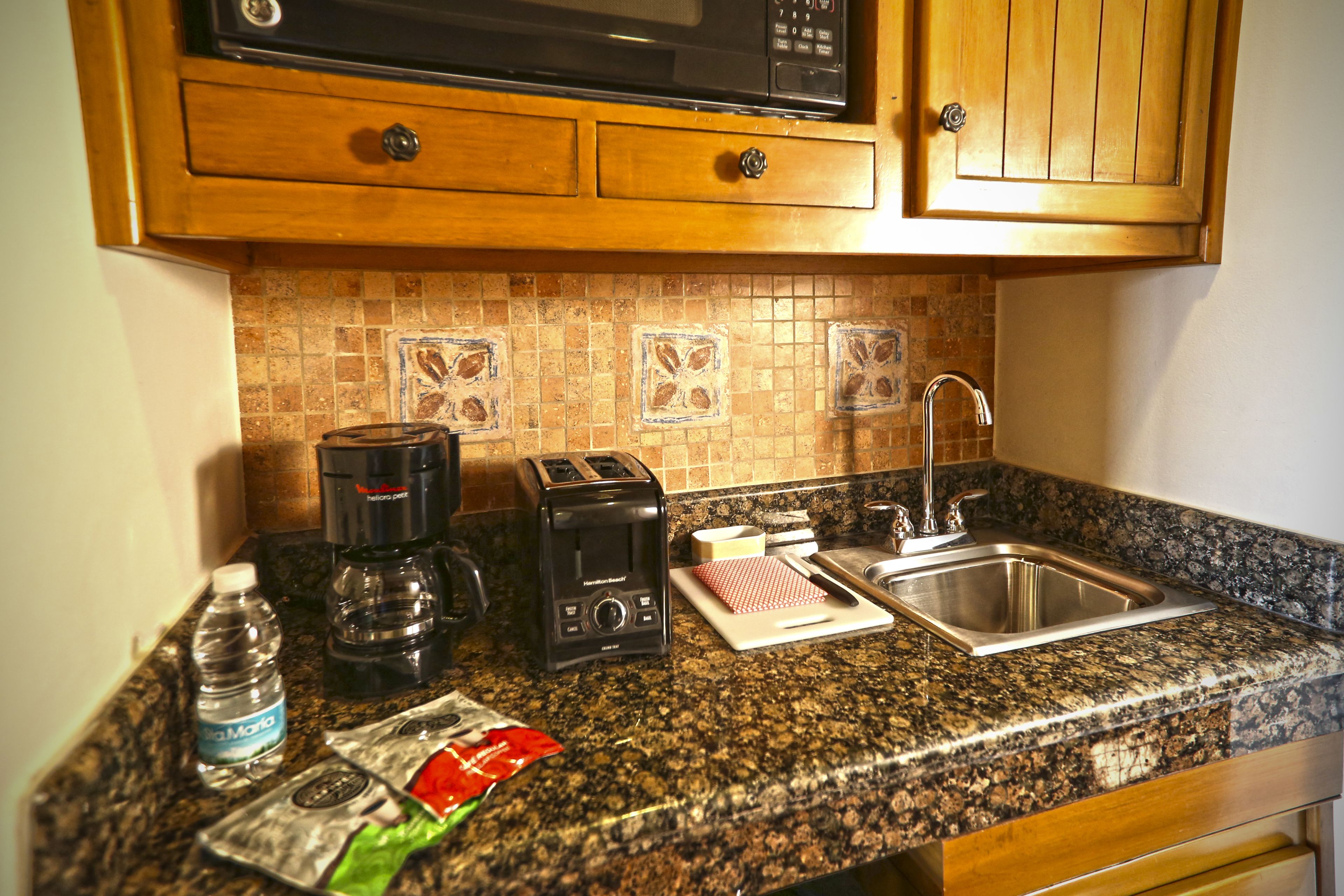 A kitchen with a granite countertop, a toaster, a coffee maker, a sink, and wooden cabinets.