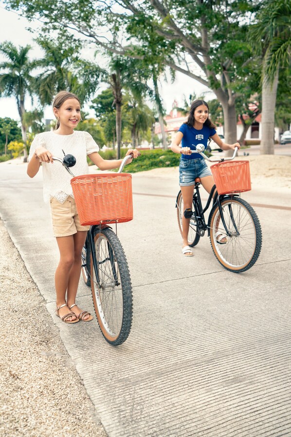 Two people riding bicycles on a paved path with trees and buildings in the background. - Holiday Inn Club Vacations The Royal Haciendas by IHG - All inclusive (Playa del Carmen)