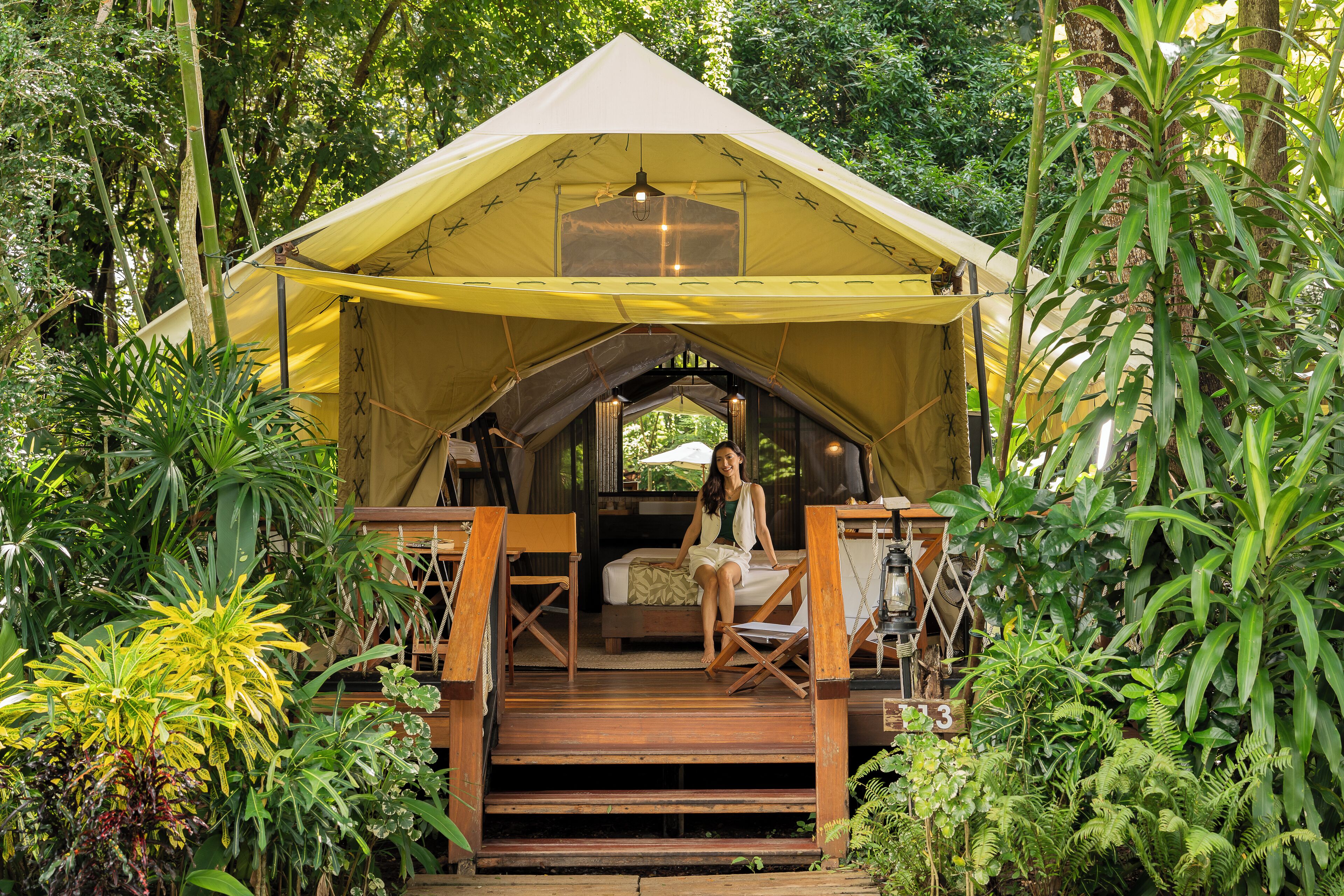 Uma tenda com deck de madeira e cama, cercada por vegetação exuberante.