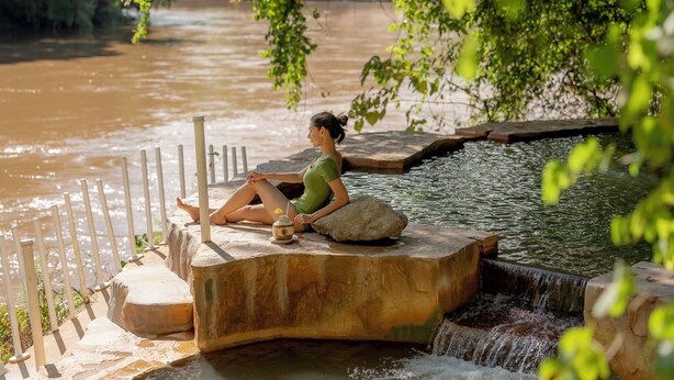 Una persona sentada junto a una fuente de agua con un borde de piedra y una pequeña cascada.