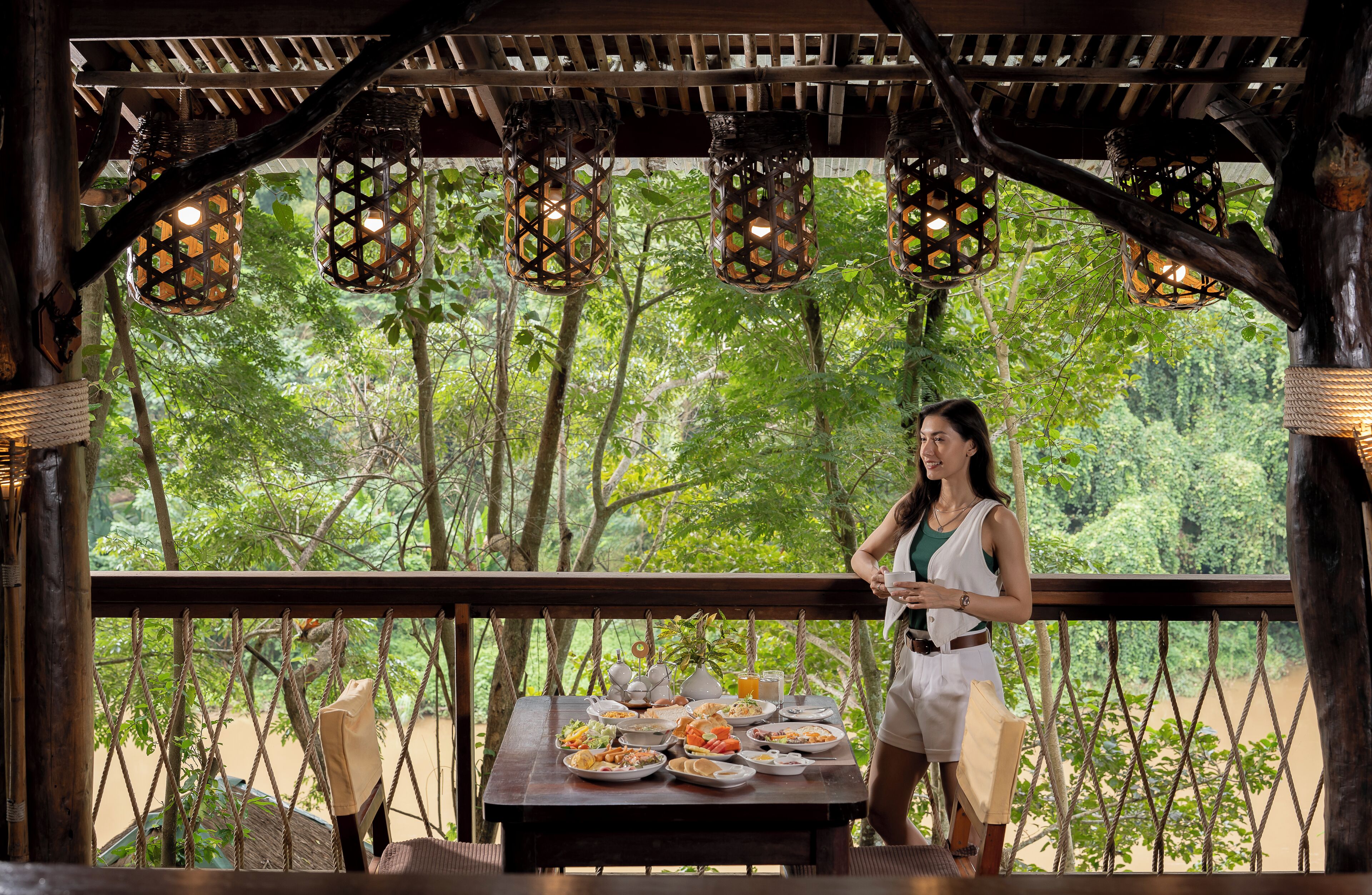 A wooden deck with a table set for a meal, surrounded by trees and hanging lanterns.