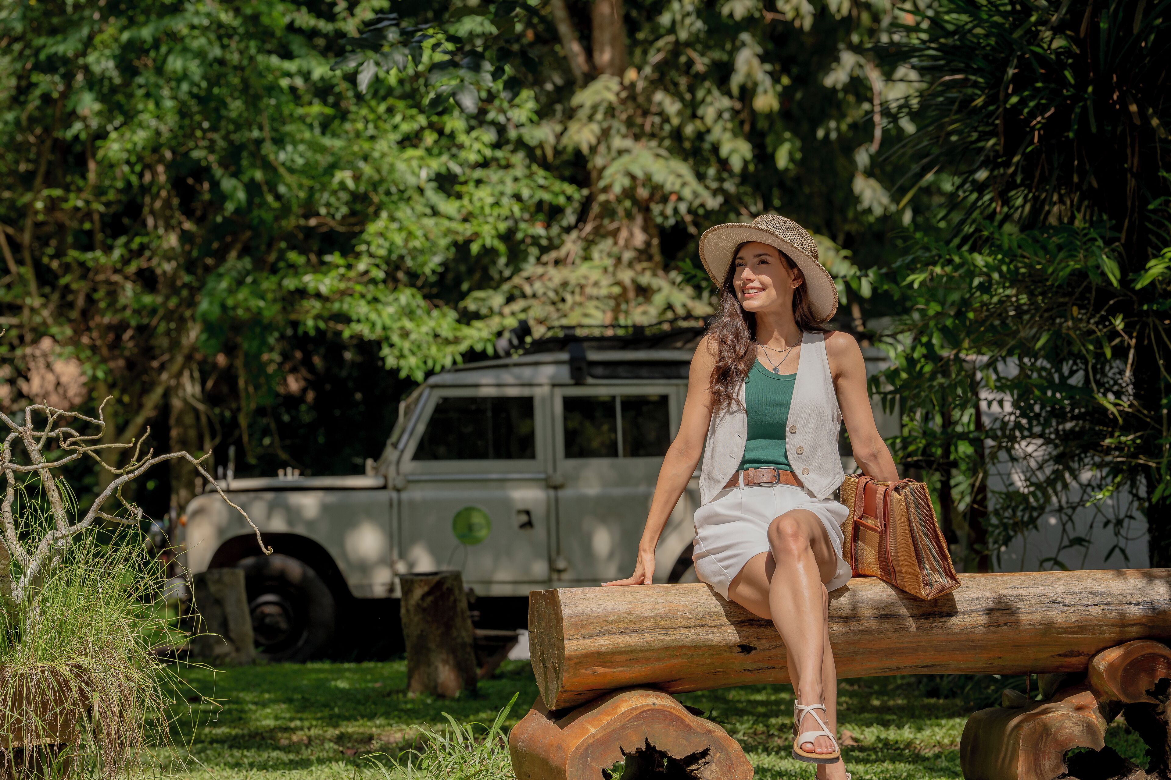 A person sitting on a log in a natural setting with a vehicle in the background.