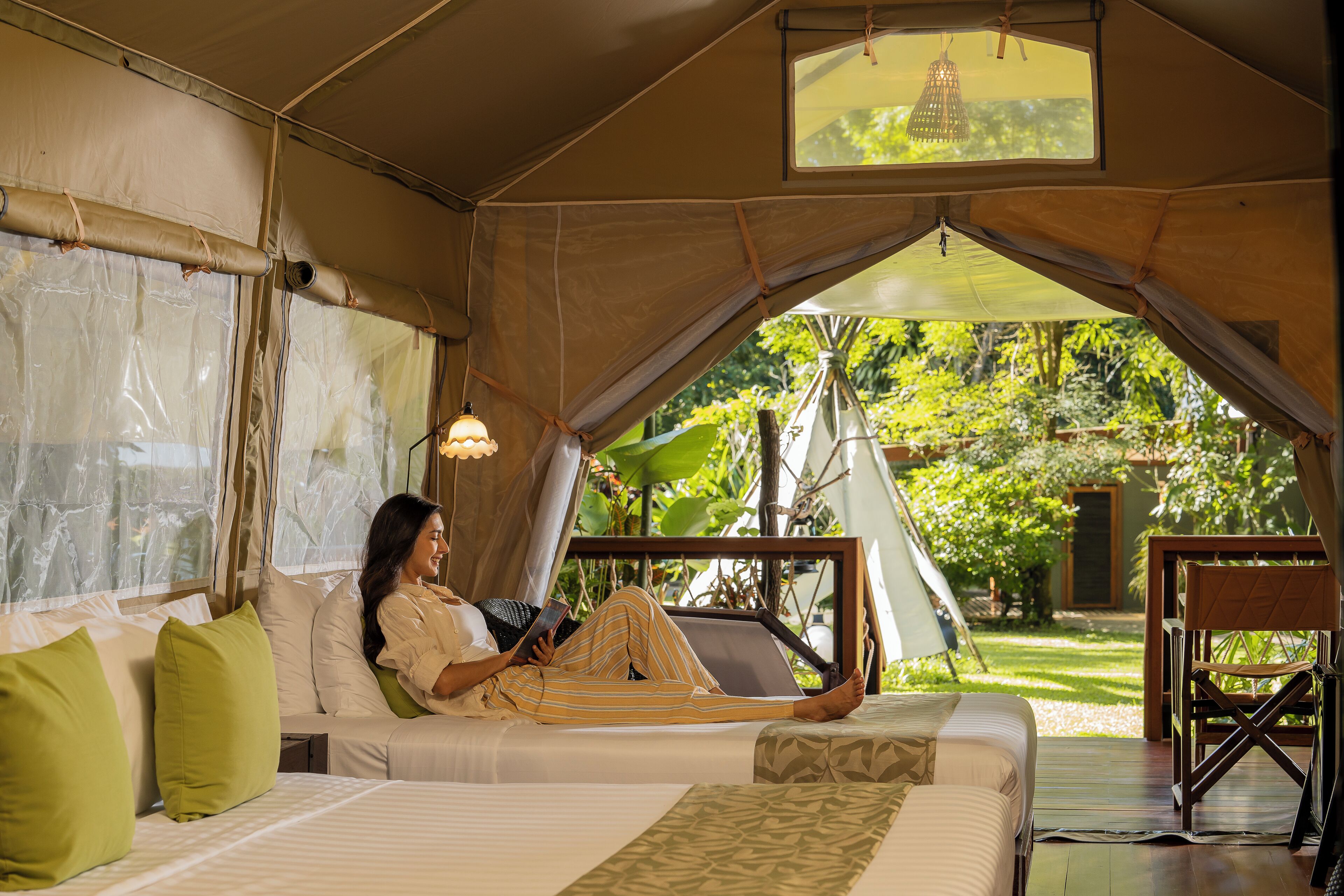 A tented accommodation with a bed, pillows, and a reading light.