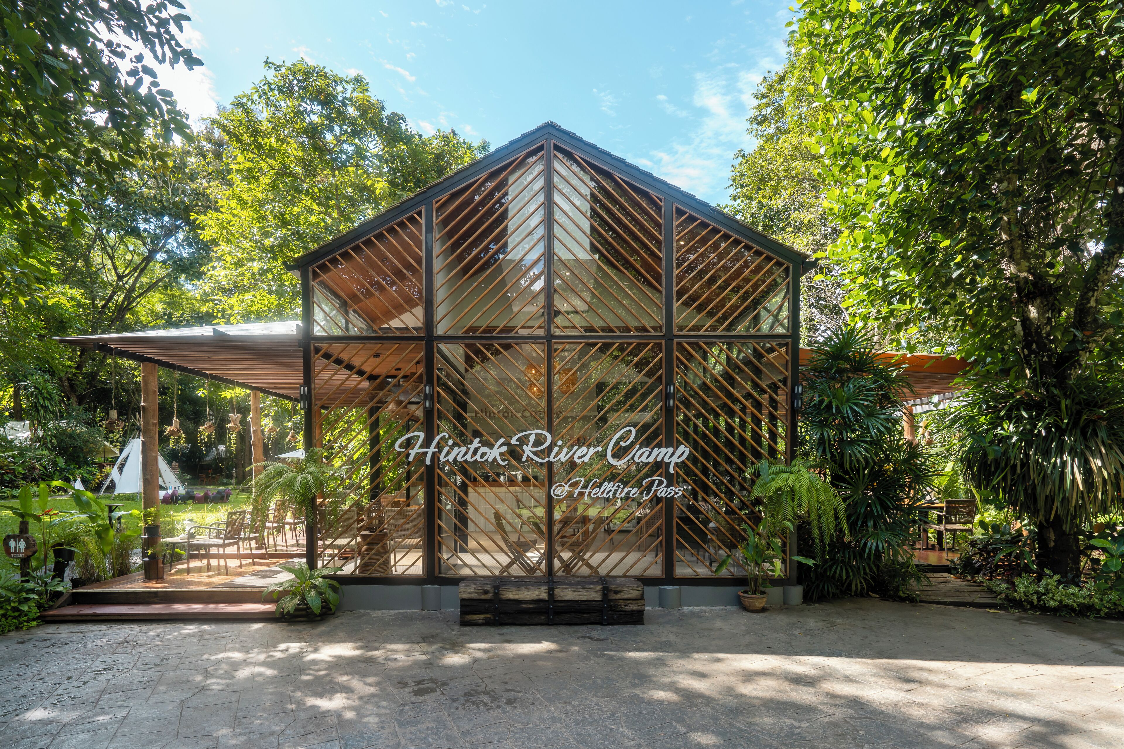 A glass-roofed structure with the text "Hintok River Camp @ Hellfire Pass" and a bench in front.