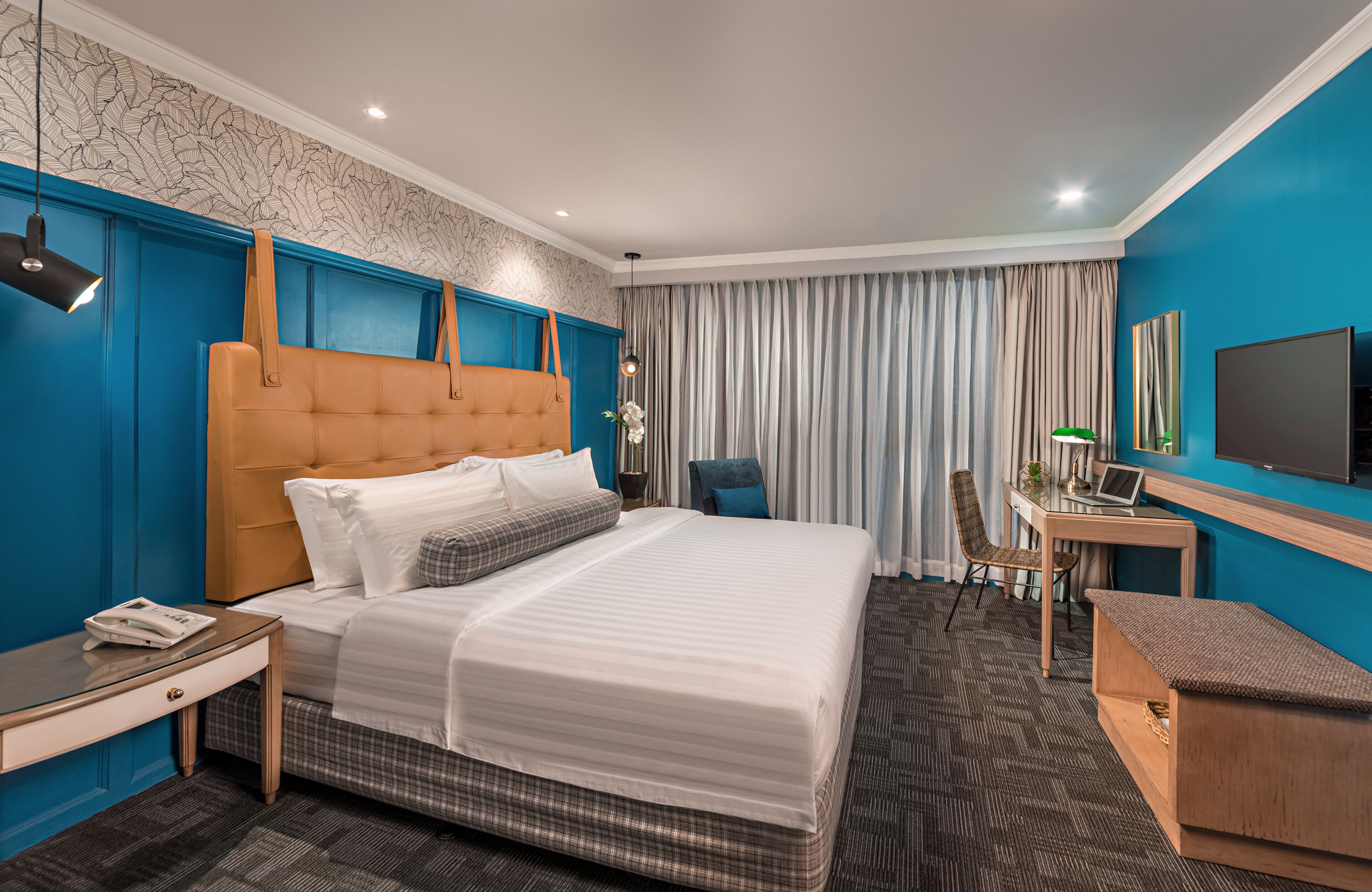 A hotel room with a large bed, a desk with a laptop, a TV, and a chair.