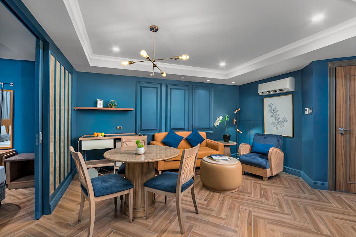 A modern living room with a herringbone wood floor, a round wooden table, and blue upholstered chairs.