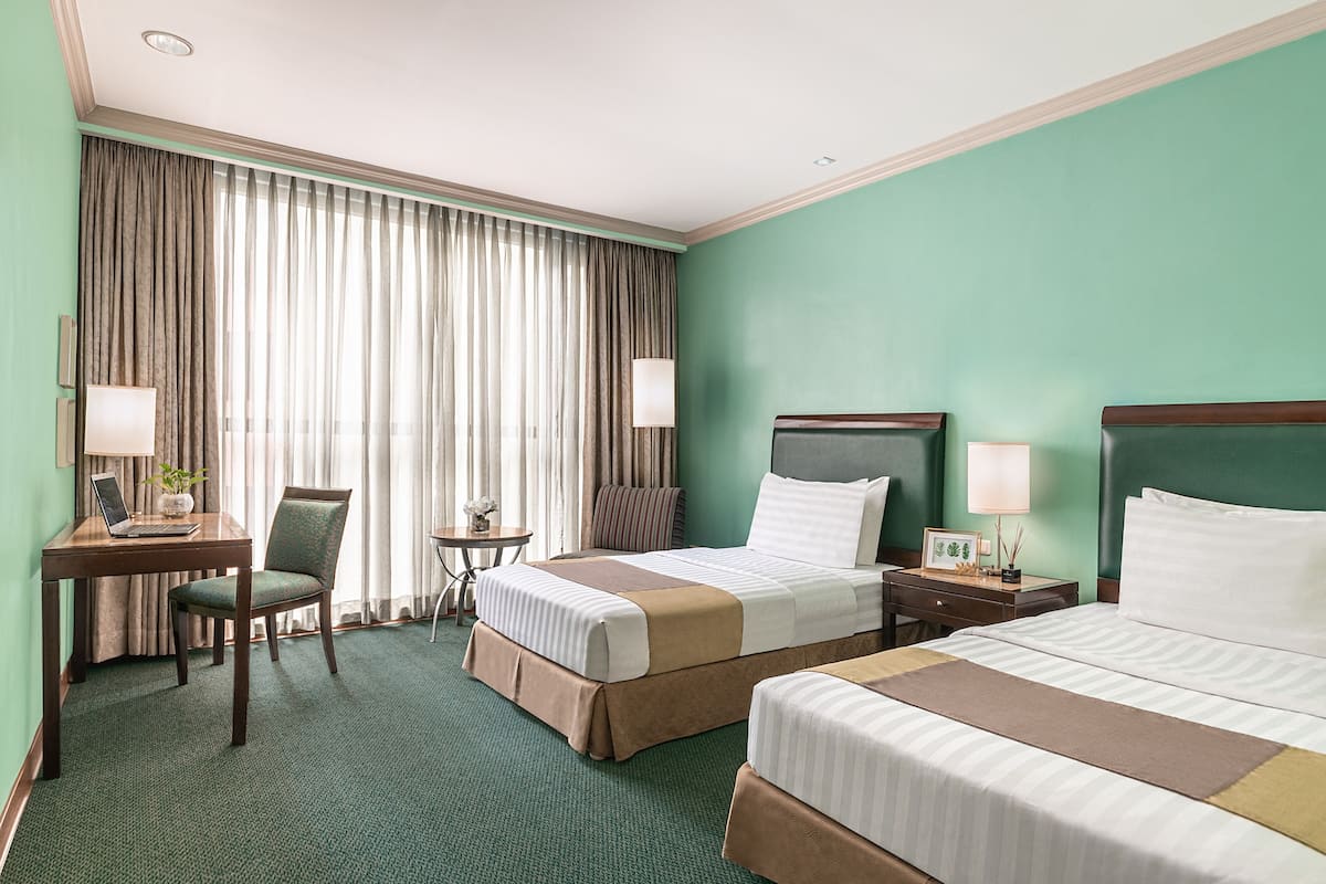A hotel room with two beds, a desk, a chair, a small table, and a large window with curtains.