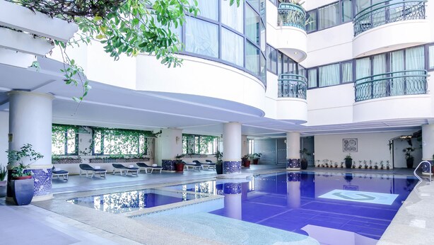 A modern indoor swimming pool with lounge chairs and potted plants. - Makati Palace Hotel (Makati)