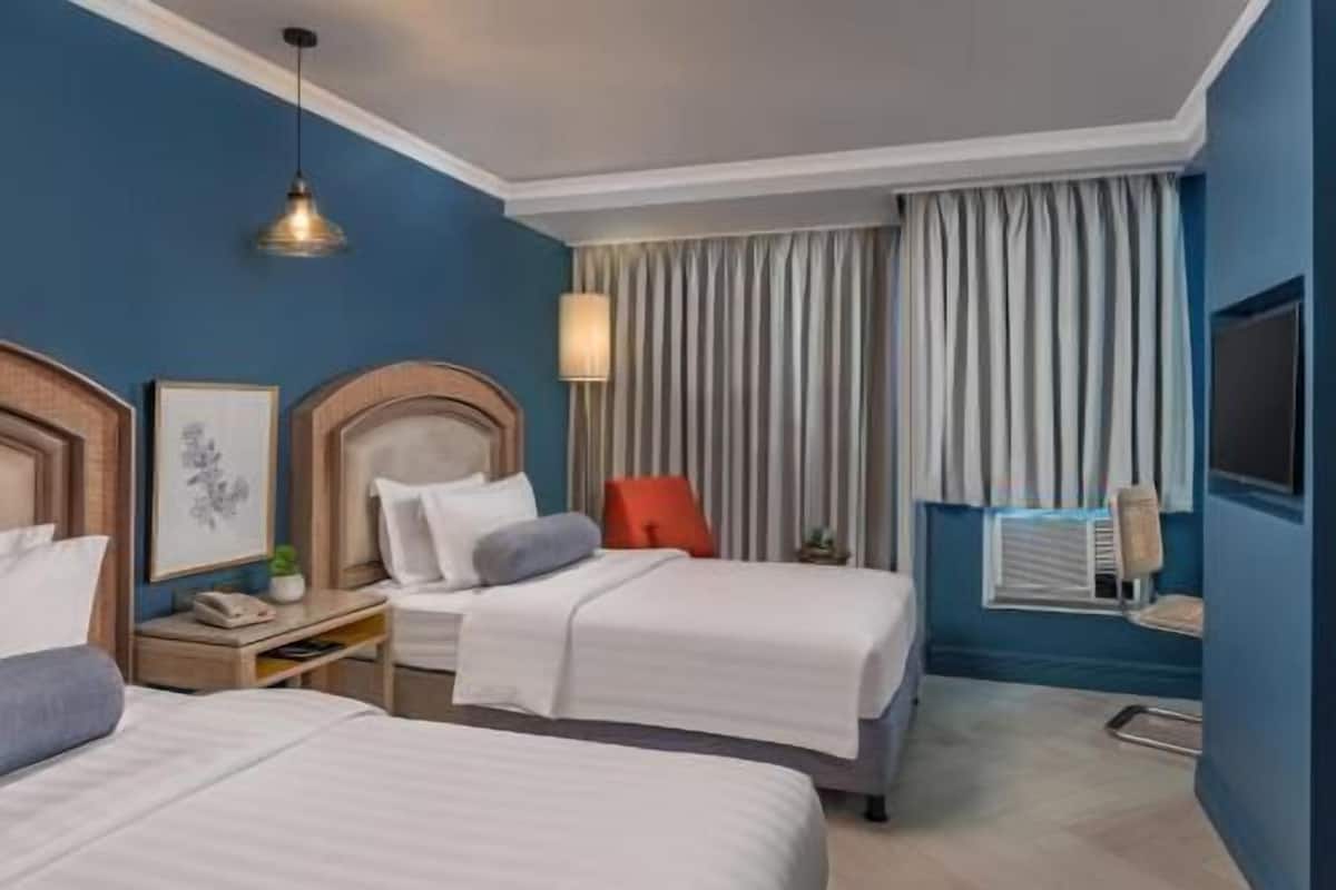 A hotel room with two beds, a desk, a chair, a TV, and a window with curtains.