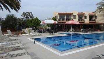 A swimming pool with lounge chairs and umbrellas, surrounded by buildings with balconies.