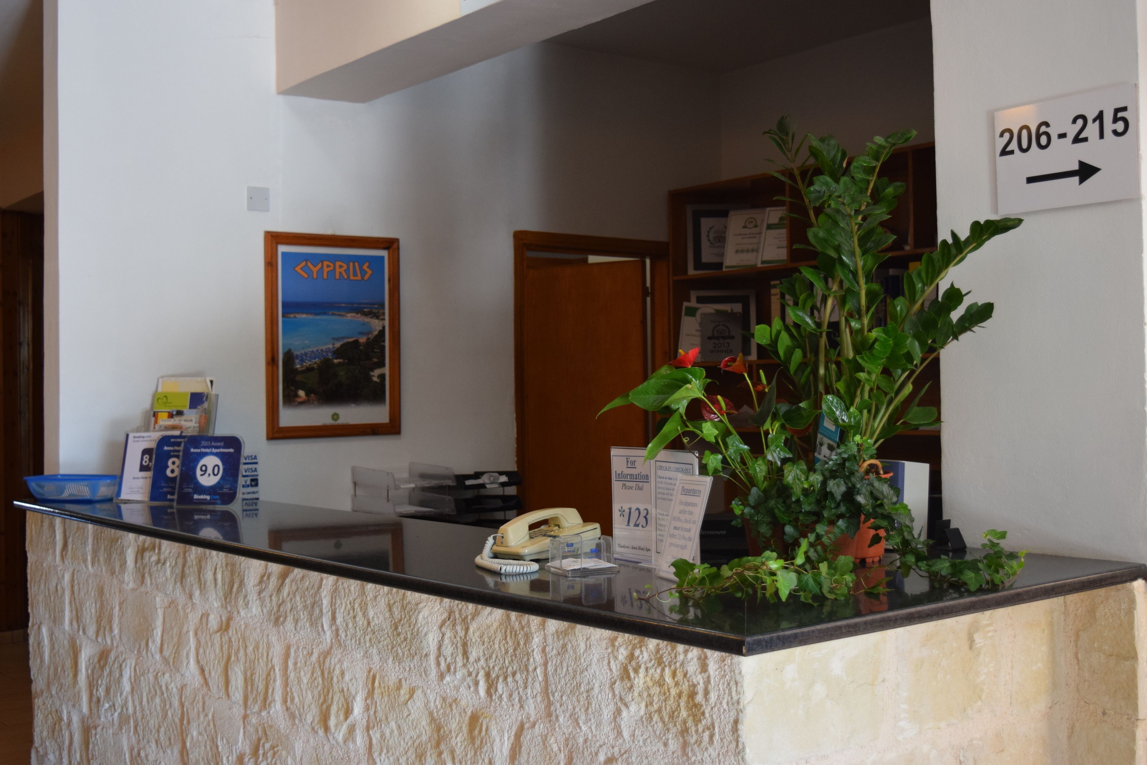 Un comptoir d’accueil orné d’une affiche représentant Chypre, d’une plante, d’un téléphone et de quelques cartes d’information.