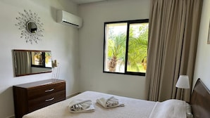 Una habitación de hotel con cama, cómoda, espejo, ventana con cortinas y lámpara.
