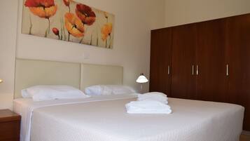 A hotel room with a large bed, a wooden wardrobe, a painting of flowers on the wall, and a bedside lamp.