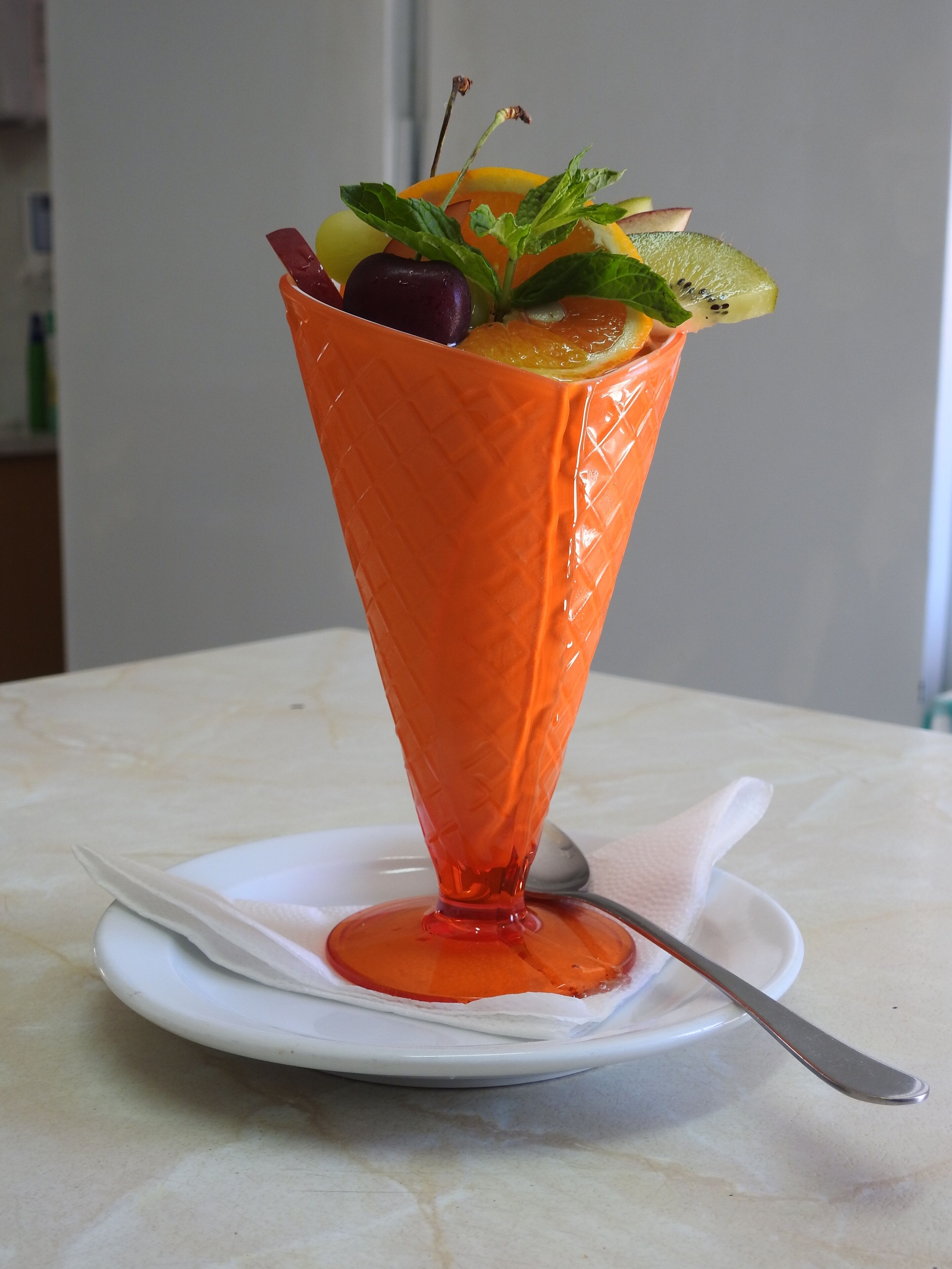 Un postre en un cono de vidrio sobre un plato blanco, con una cuchara.