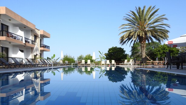 Una piscina con sillas de descanso y sombrillas, rodeada de palmeras y edificios.