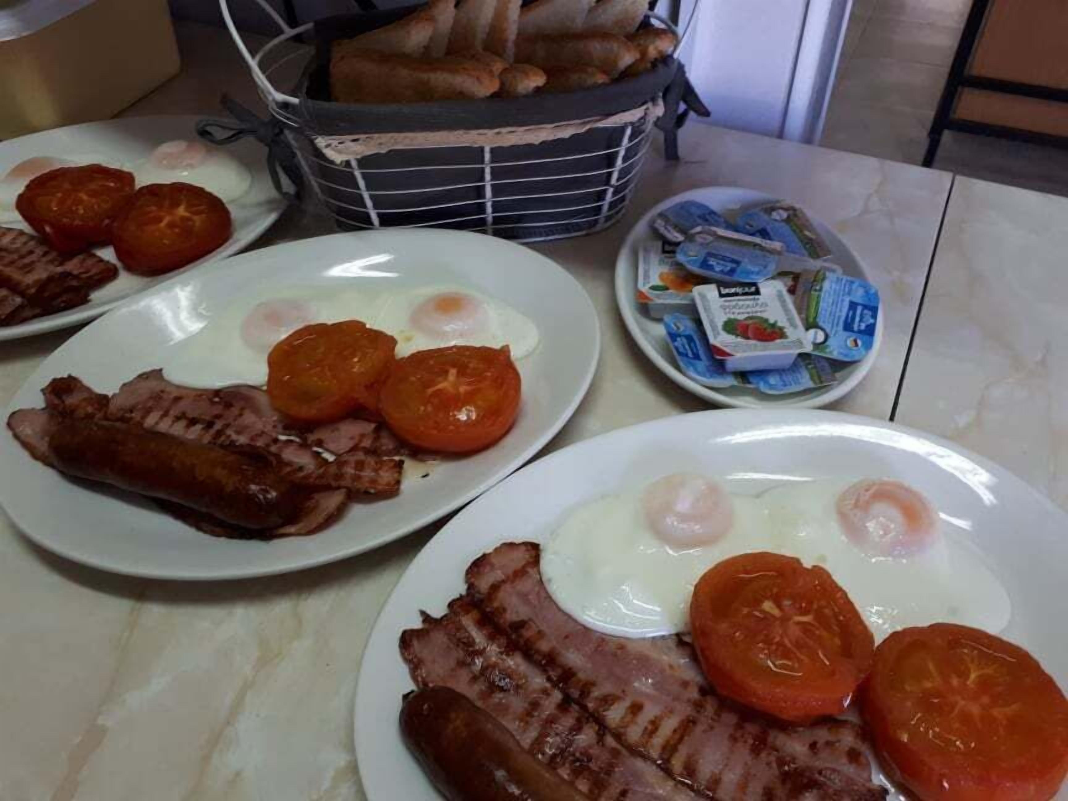 A breakfast setting with plates of eggs, bacon, sausages, and tomatoes.