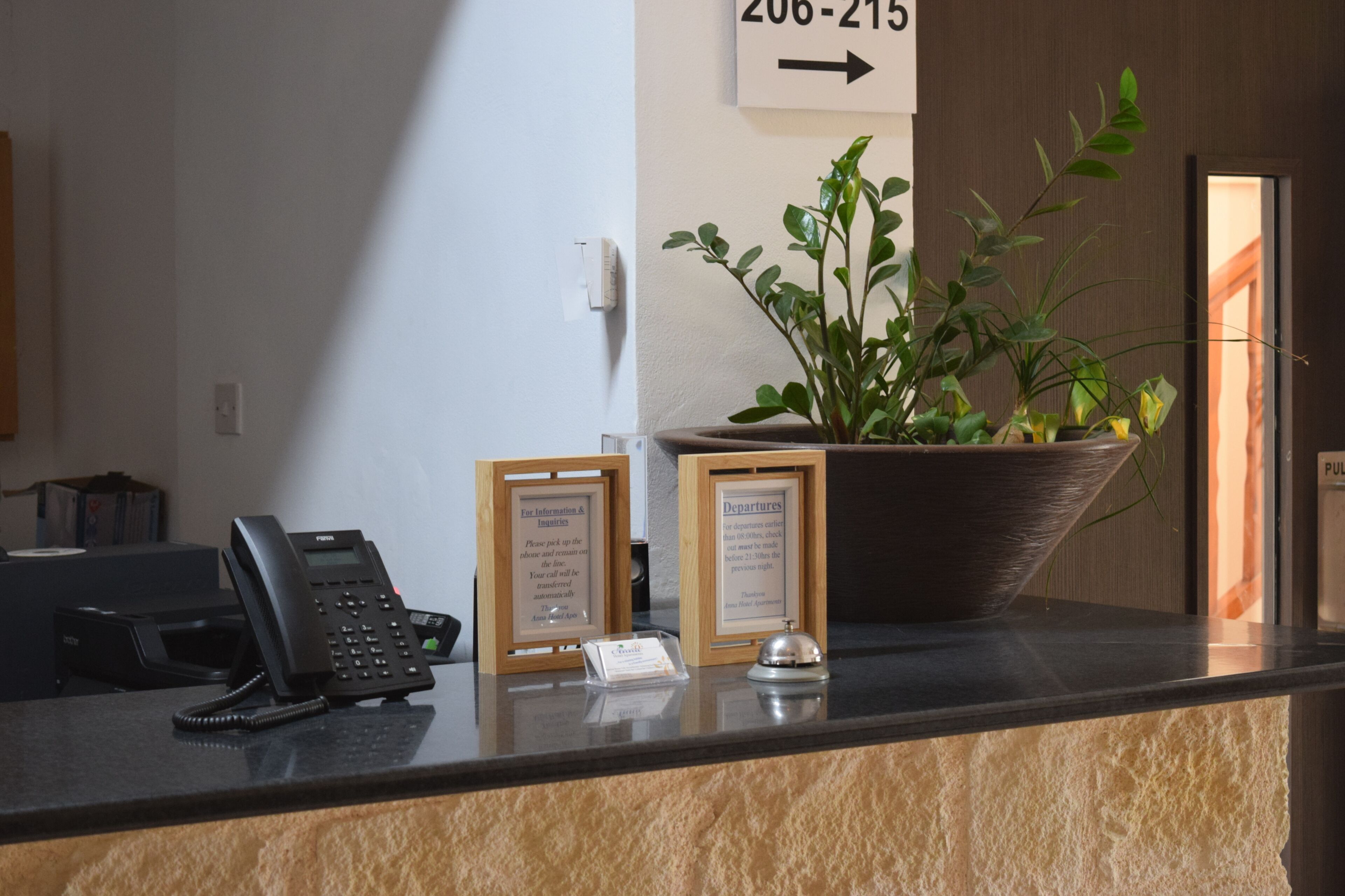 Un comptoir d’accueil avec un téléphone, des panneaux d’information encadrés, une plante en pot et un panneau indicateur.