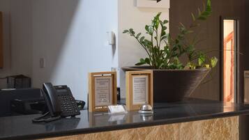 Un comptoir d’accueil avec un téléphone, des panneaux d’information encadrés, une plante en pot et un panneau indicateur.