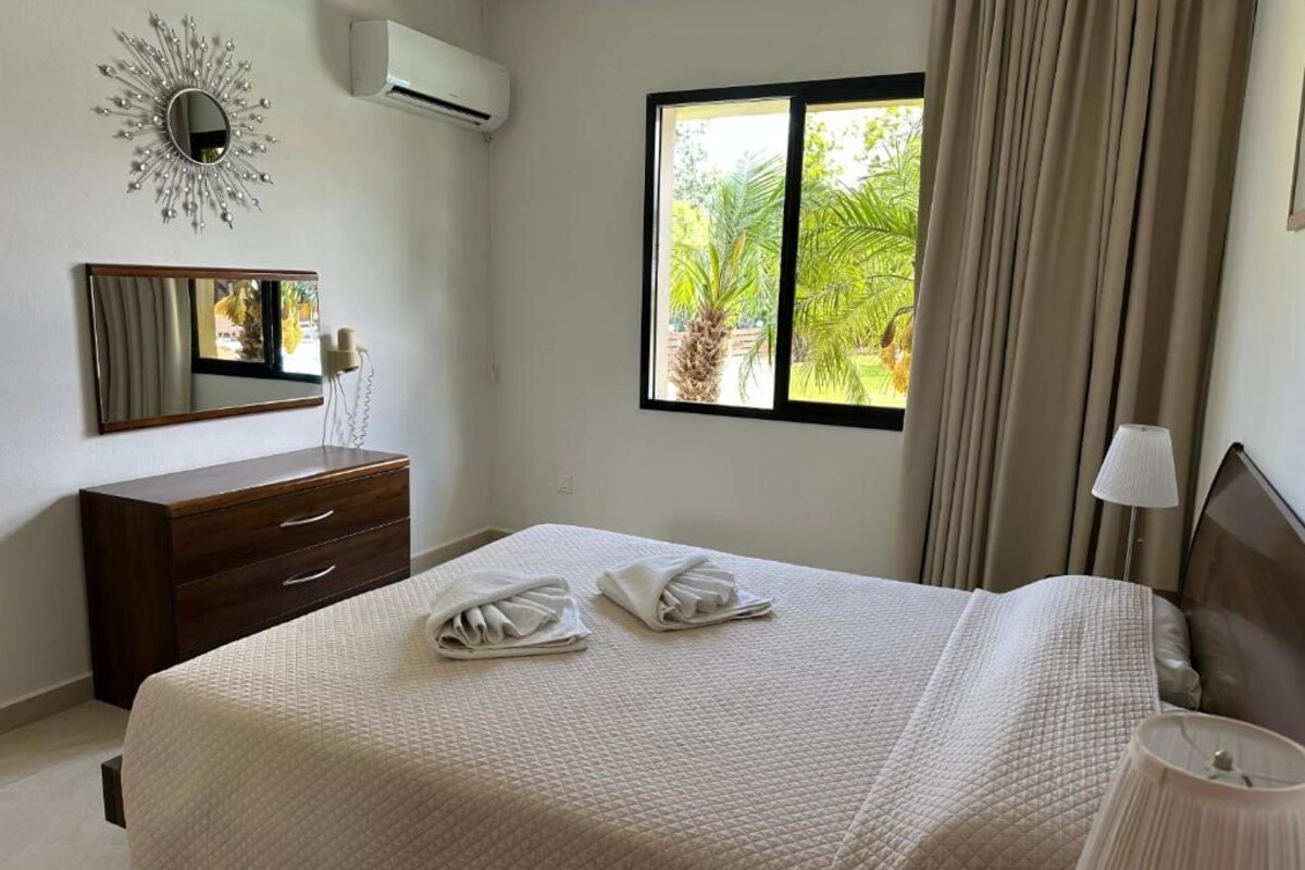 Una habitación de hotel con cama, cómoda, espejo, ventana con cortinas y lámpara.