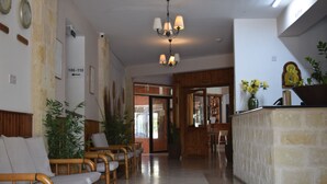 Zona de recepción con mostrador, sillas, candelabro y una pared con un reloj y señalización.