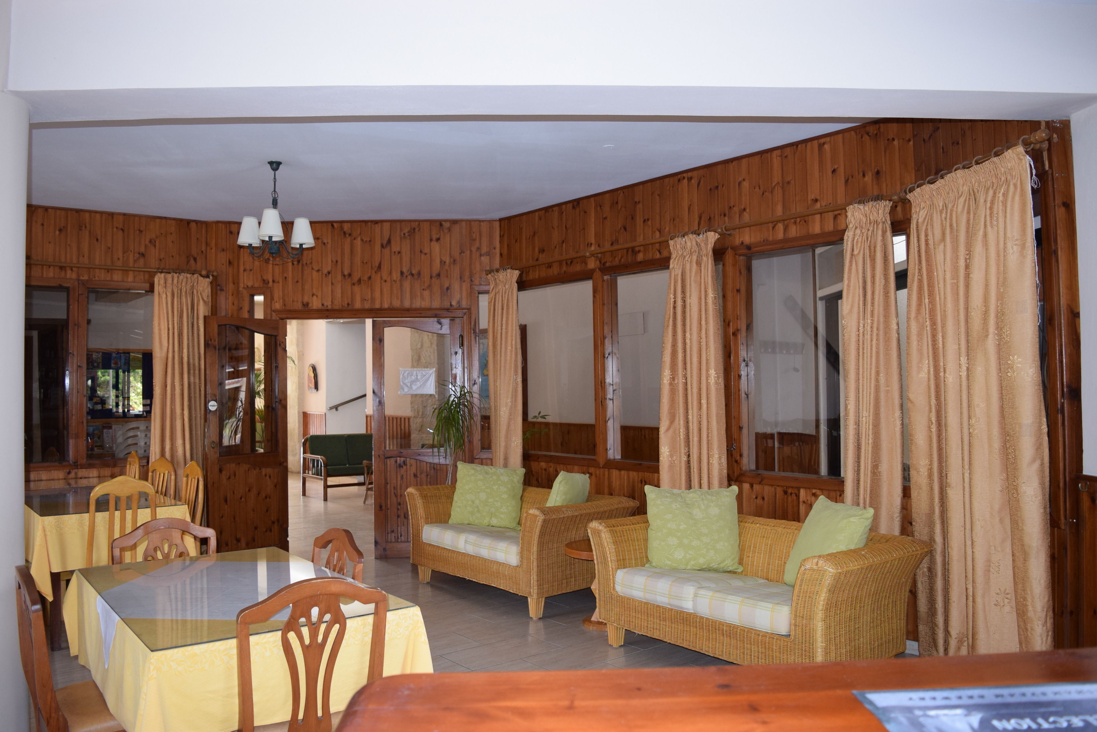 Ein Zimmer mit Holzwänden, einem Esstisch mit Stühlen, zwei Sofas mit Kissen und einer Chandelüster.