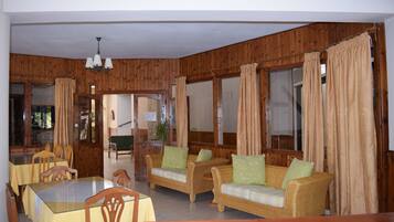 Ein Zimmer mit Holzwänden, einem Esstisch mit Stühlen, zwei Sofas mit Kissen und einer Chandelüster.