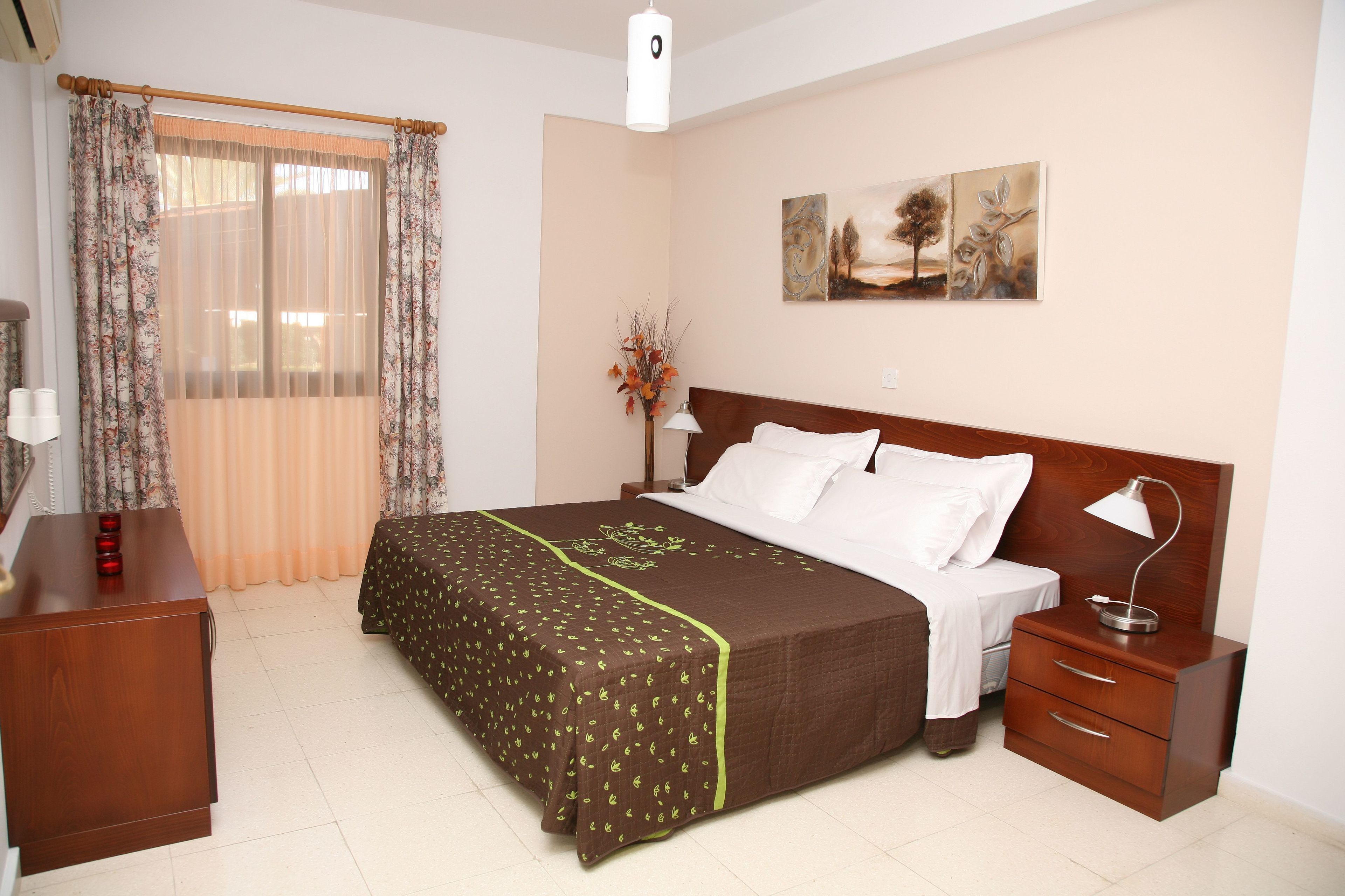 A neatly arranged bedroom with a bed, bedside tables, a lamp, and artwork on the wall.