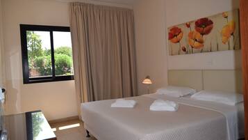 A hotel room with a bed, a window with curtains, a lamp, and a painting on the wall.
