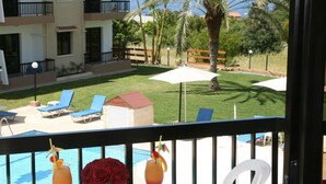 Un balcón con piscina, sillones de descanso y una mesa con bebidas y flores.