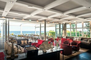 Amplio espacio interior con vista al mar, con asientos en rojo y beige, una gran decoración de ancla y una mesa de madera.