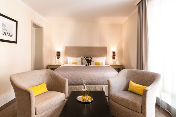 A hotel room with a large bed, two armchairs, a small table with a bottle and glasses, and a framed picture on the wall. - Strandhotel Ostseeblick (Heringsdorf)