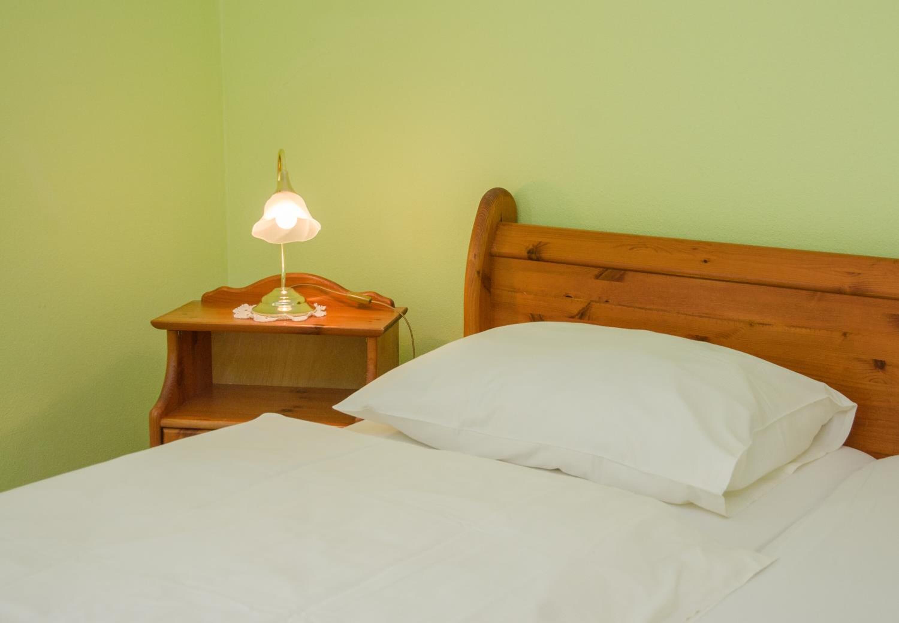 A bed with white sheets and pillows, a wooden headboard, and a nightstand with a lamp.