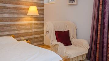 A bedroom with a wooden wall, a bed, a chair with a red pillow, a floor lamp, and curtains.