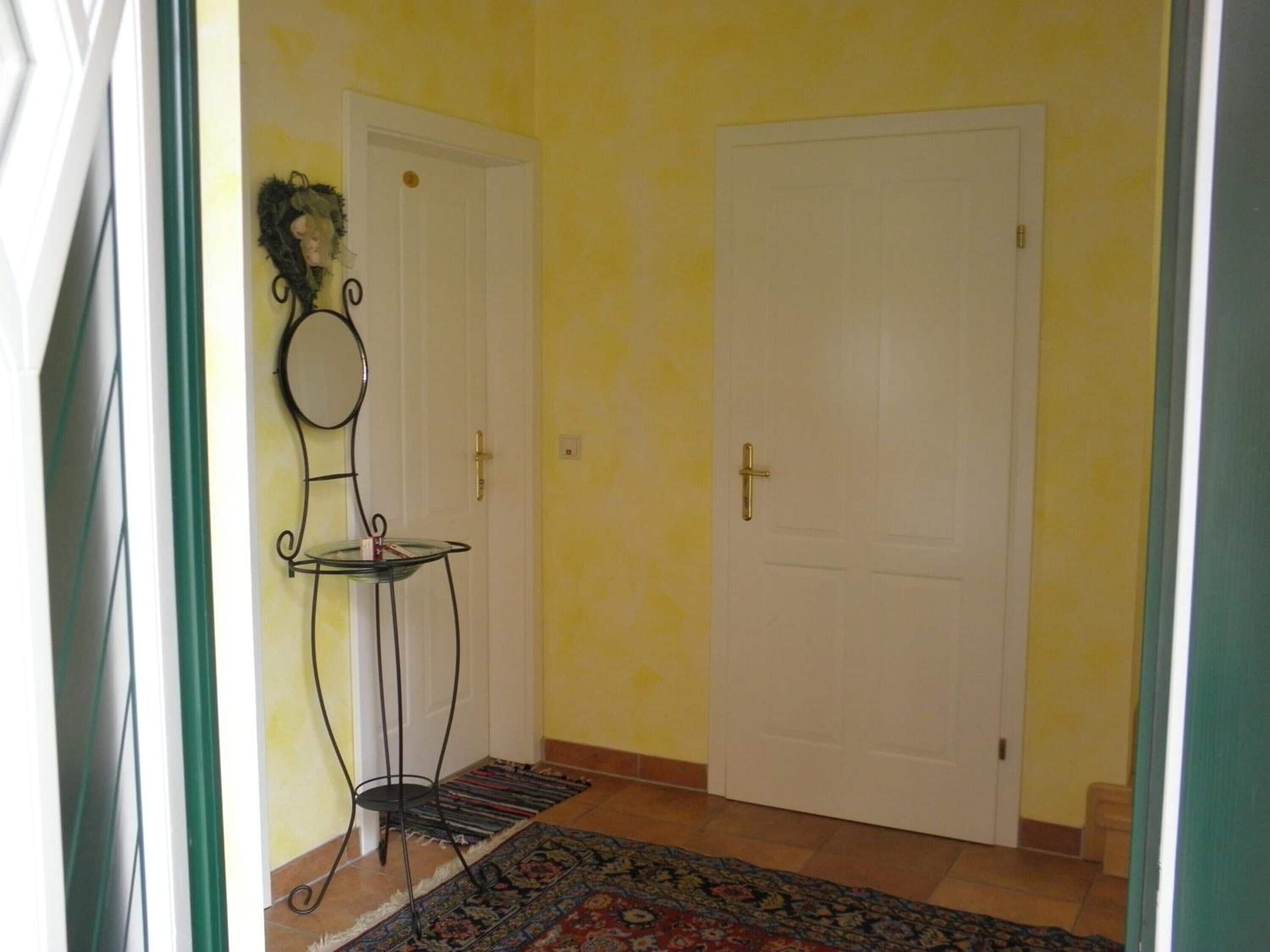 A hallway with two white doors, a small glass table with a metal frame, and a patterned rug on the floor.