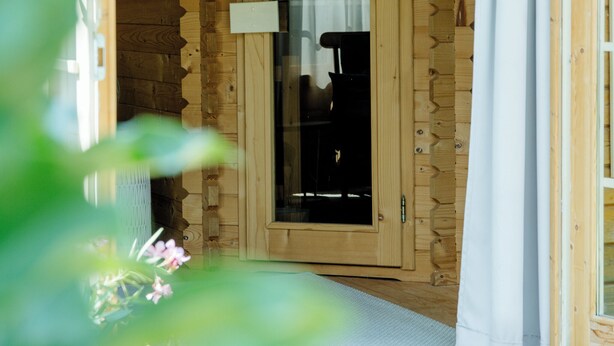 Der Eingang einer Holzhütte mit Tür, kleinem Fenster und weißem Vorhang.