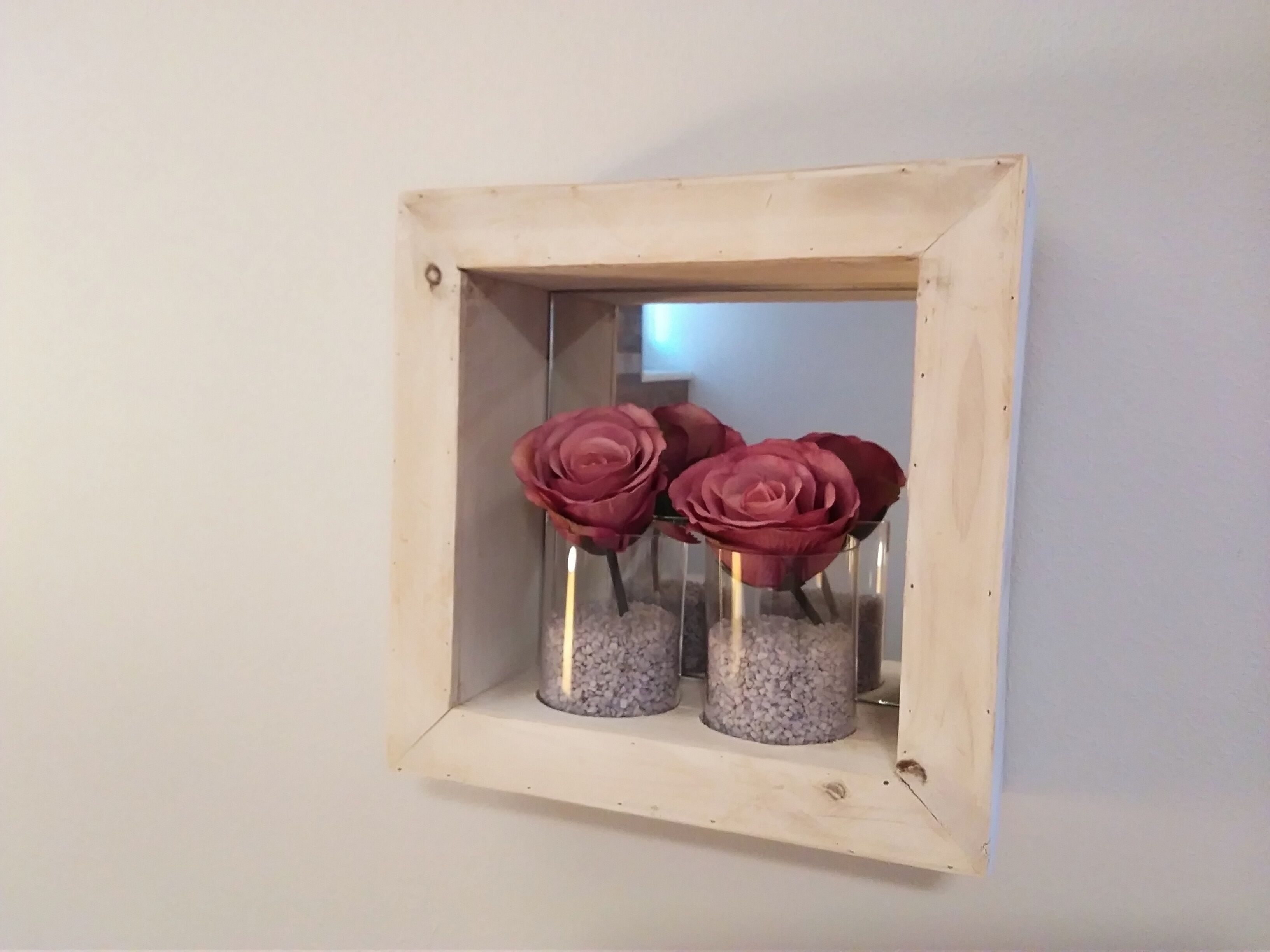 A square mirror with a light frame on a wall.
