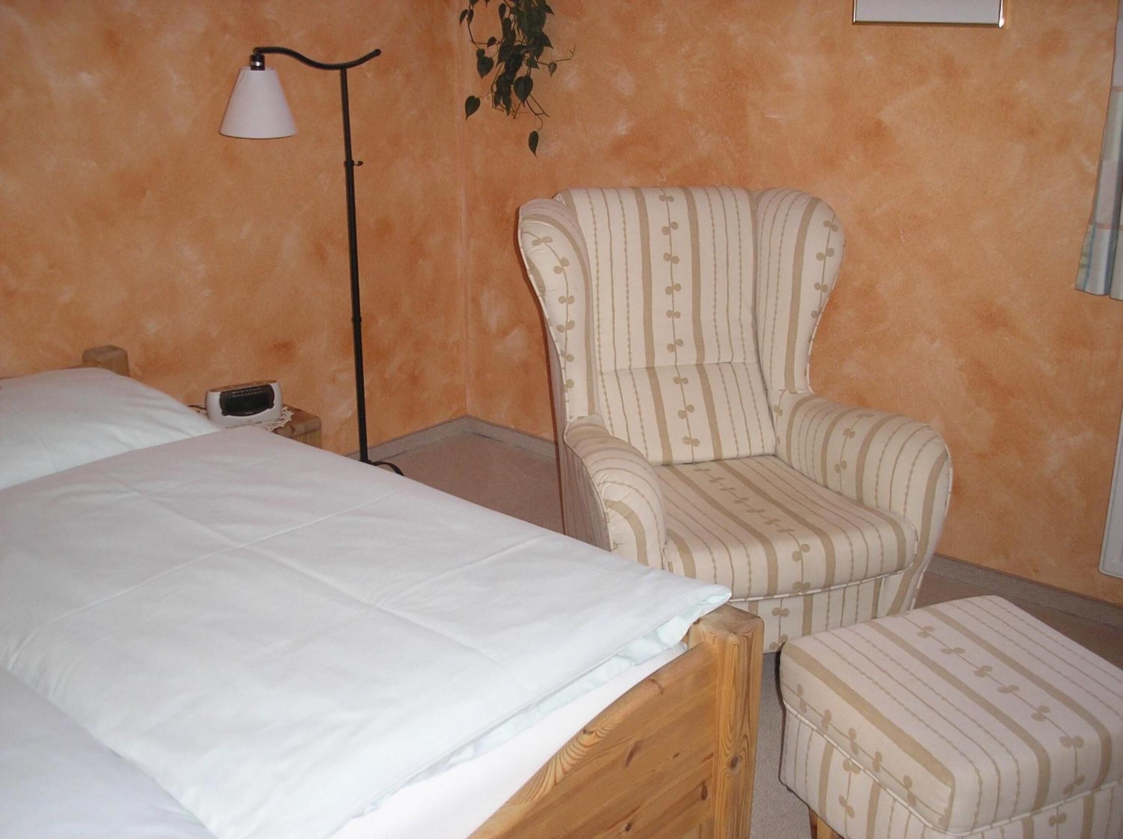 A bedroom with a bed, a bedside table, a lamp, and a striped armchair.