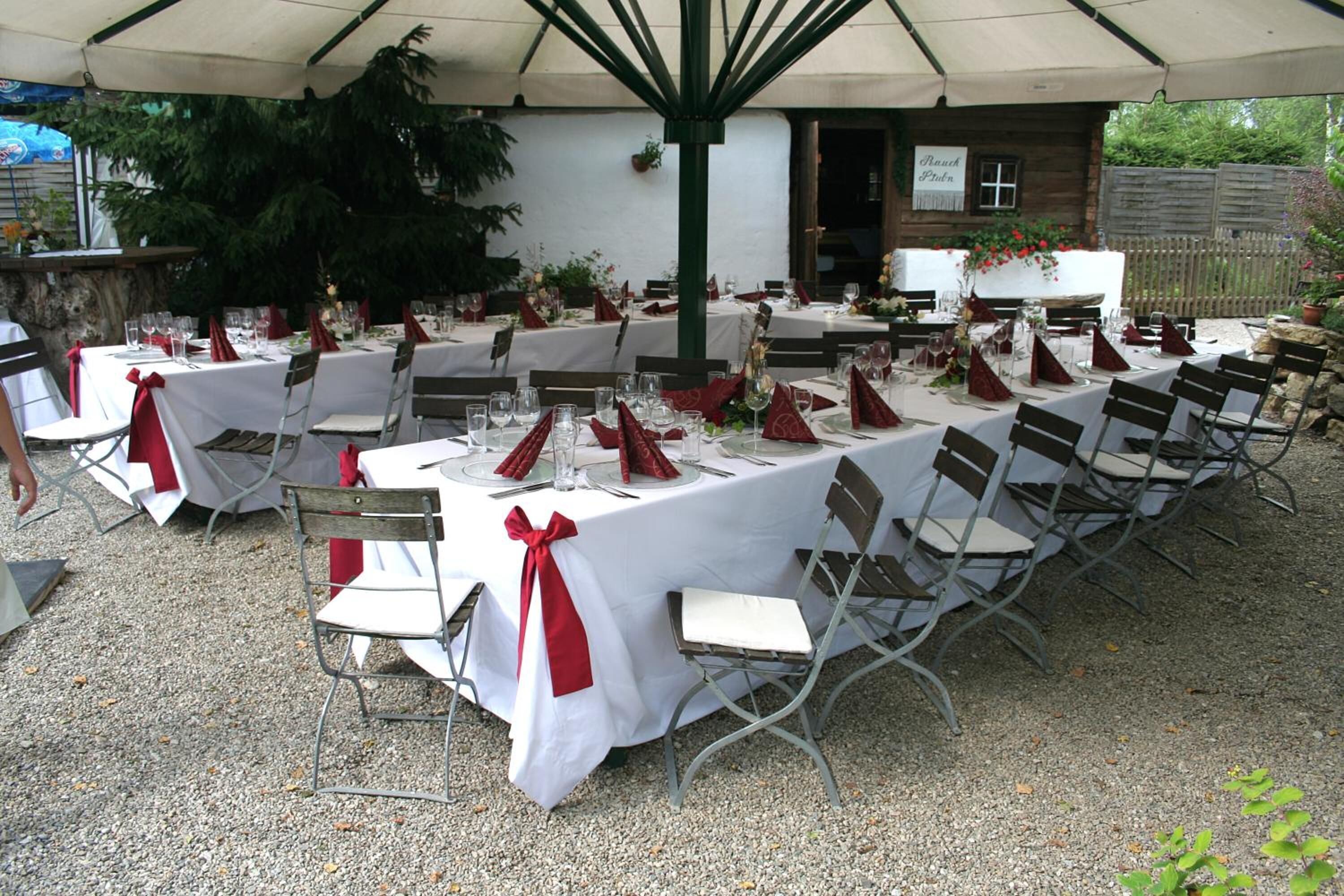 An outdoor dining area with tables set for a meal, surrounded by chairs, under a canopy.