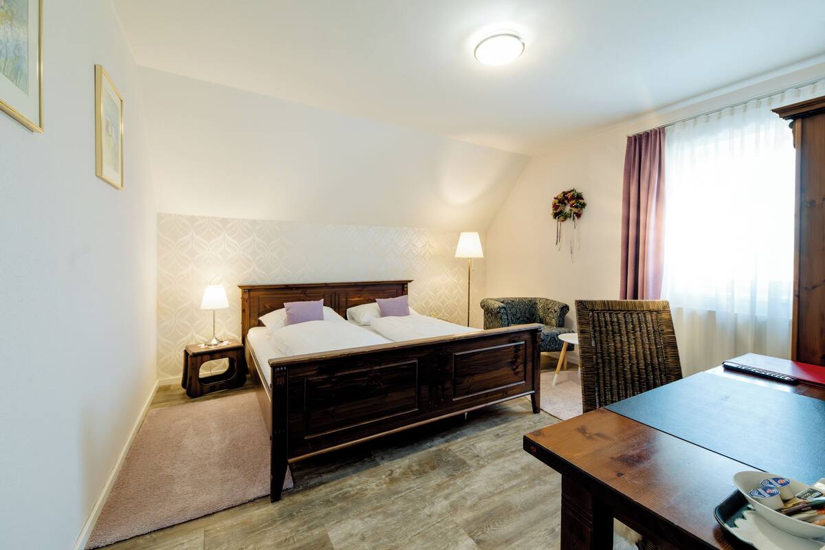 Une chambre à coucher comprenant un lit, une table de chevet, une lampe, une chaise et une table avec une télécommande.